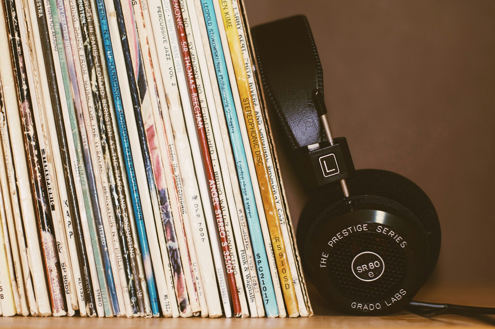 A row of vinyl LP sleeves standing upright on a shelf with a pair of Grado headphones leaning against the end of the row