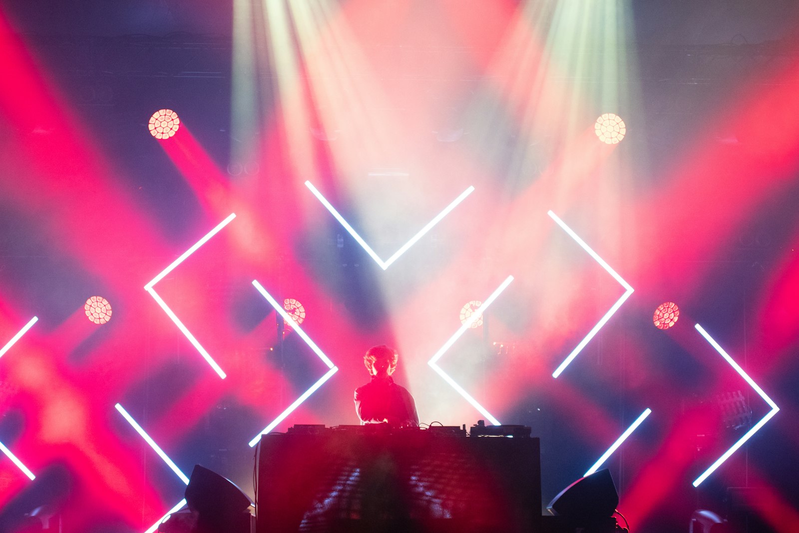 A DJ in silhouette at the decks in front of a huge LED screen showing bright pink and white geometric visuals, the kind of reactive backdrop you can render and loop for a booth screen